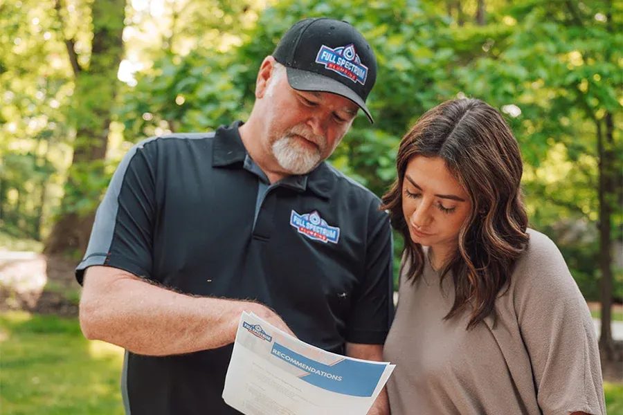 Man wearing a Full Spectrum cap and polo explains a recommendations flyer to a woman in a park.