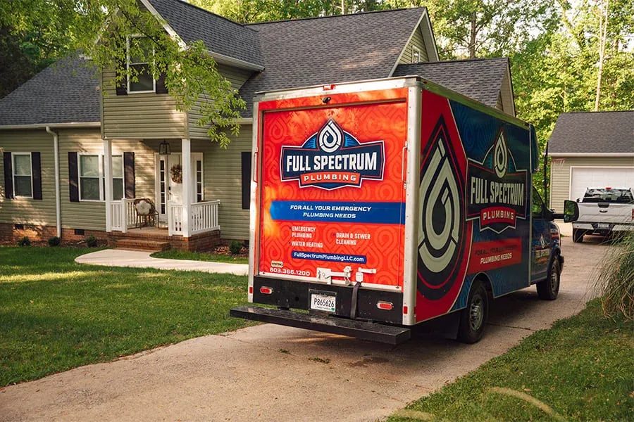 Full Spectrum Plumbing van parked in a residential driveway with a two-story house in the background.