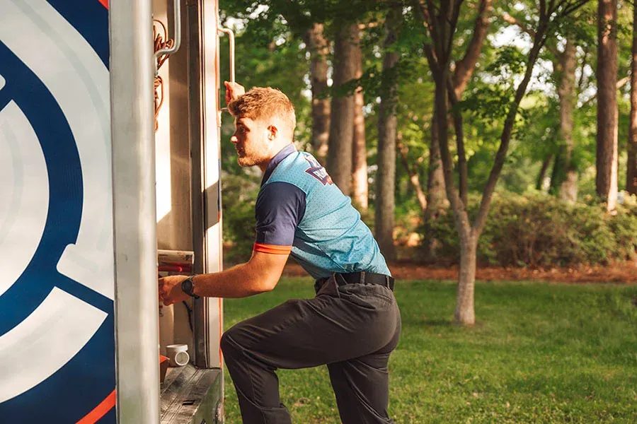 Man in a teal athletic shirt and black pants is stepping into a food truck, with a park and trees in the background.