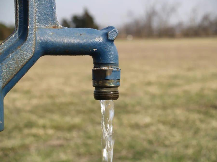 Blue outdoor faucet with steady dripping water in a grassy field, close-up view of the tap.