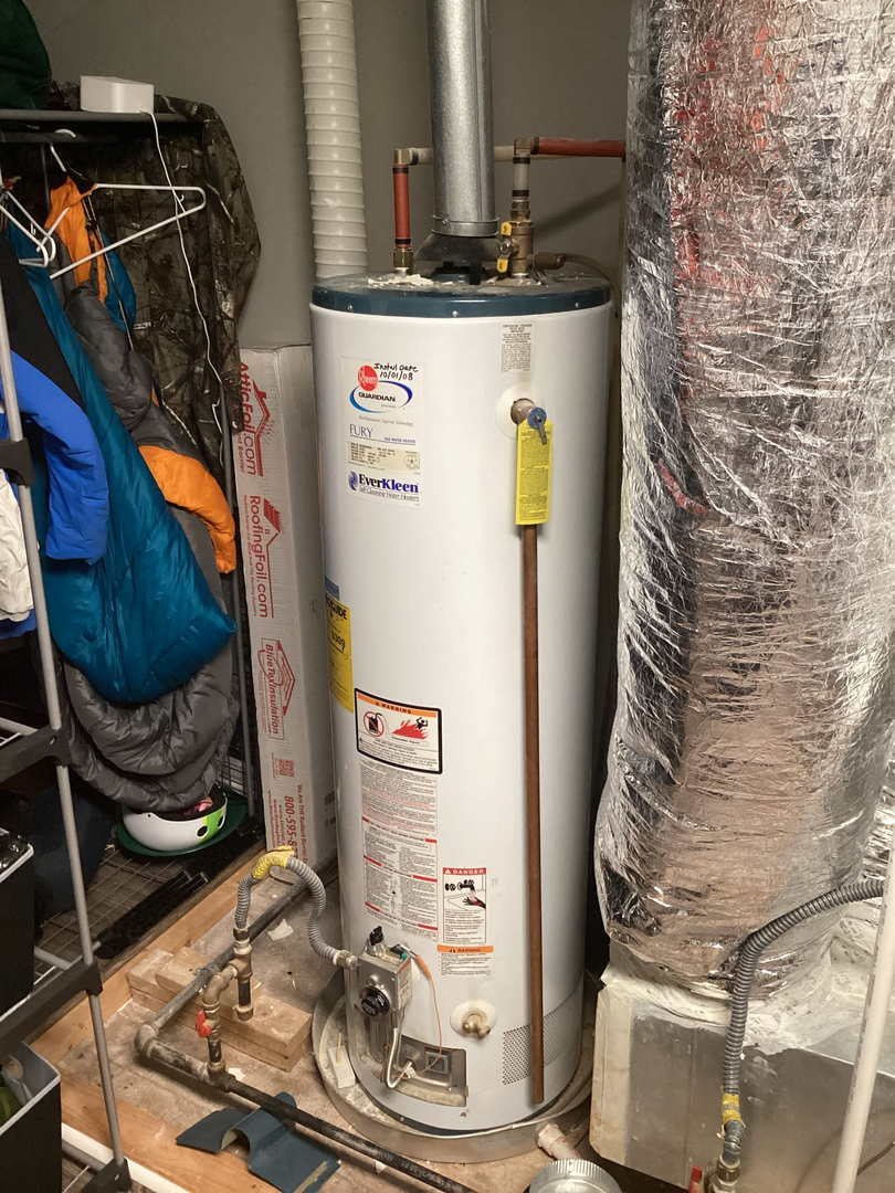 A residential water heater installed in a basement, surrounded by insulation materials and various stored items, showcasing typical plumbing in Charlotte.