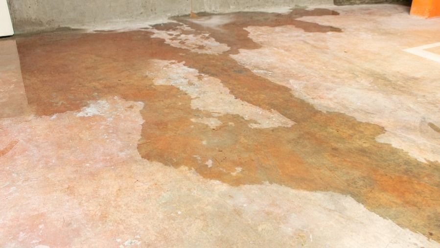 Concrete floor with large irregular brown and orange stain patches, likely damp or rust damage in a garage or industrial space